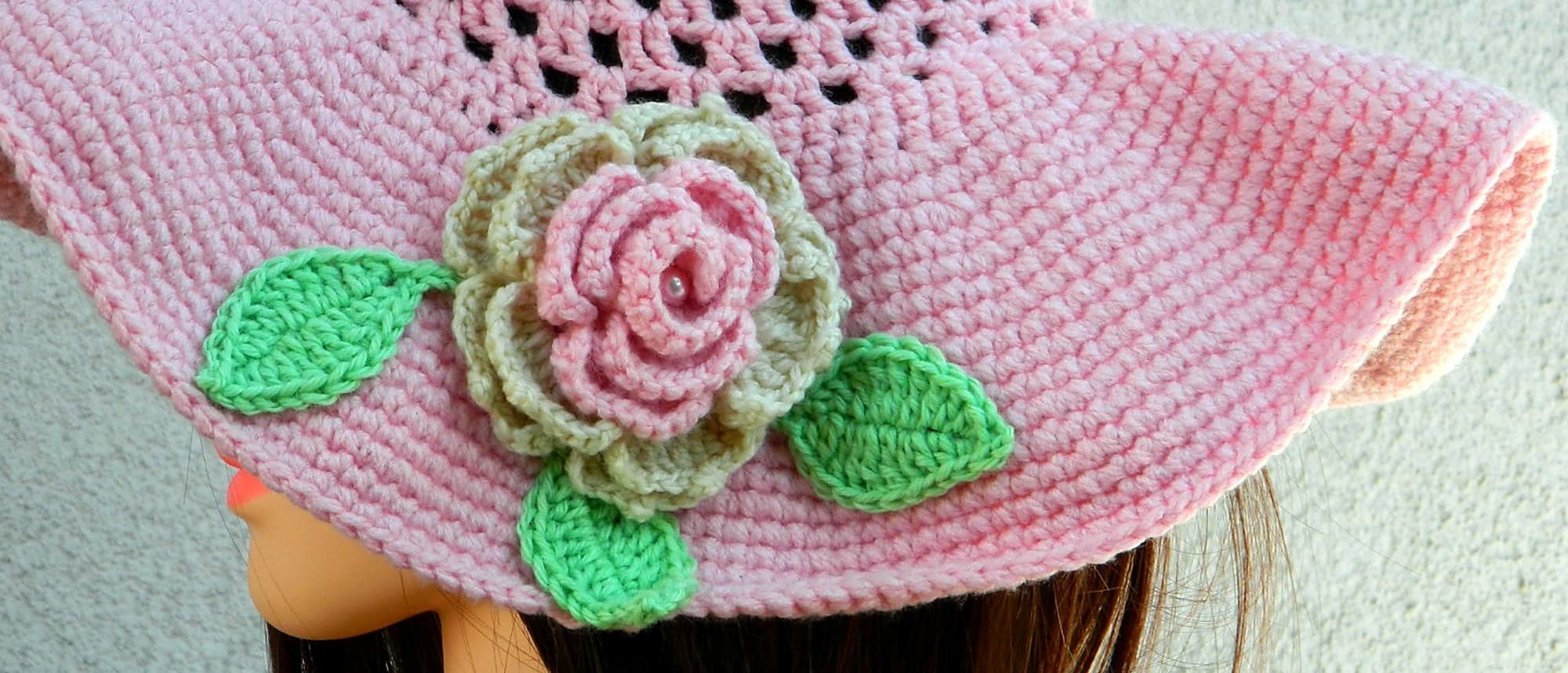 Makro: die von Hand gehäkelte Rose mit einer echten Perle im Kern auf dem rosa Sonnenhut